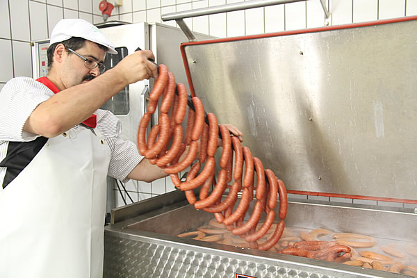 Würste werden von Hand aus dem dampfenden Kessel gehoben